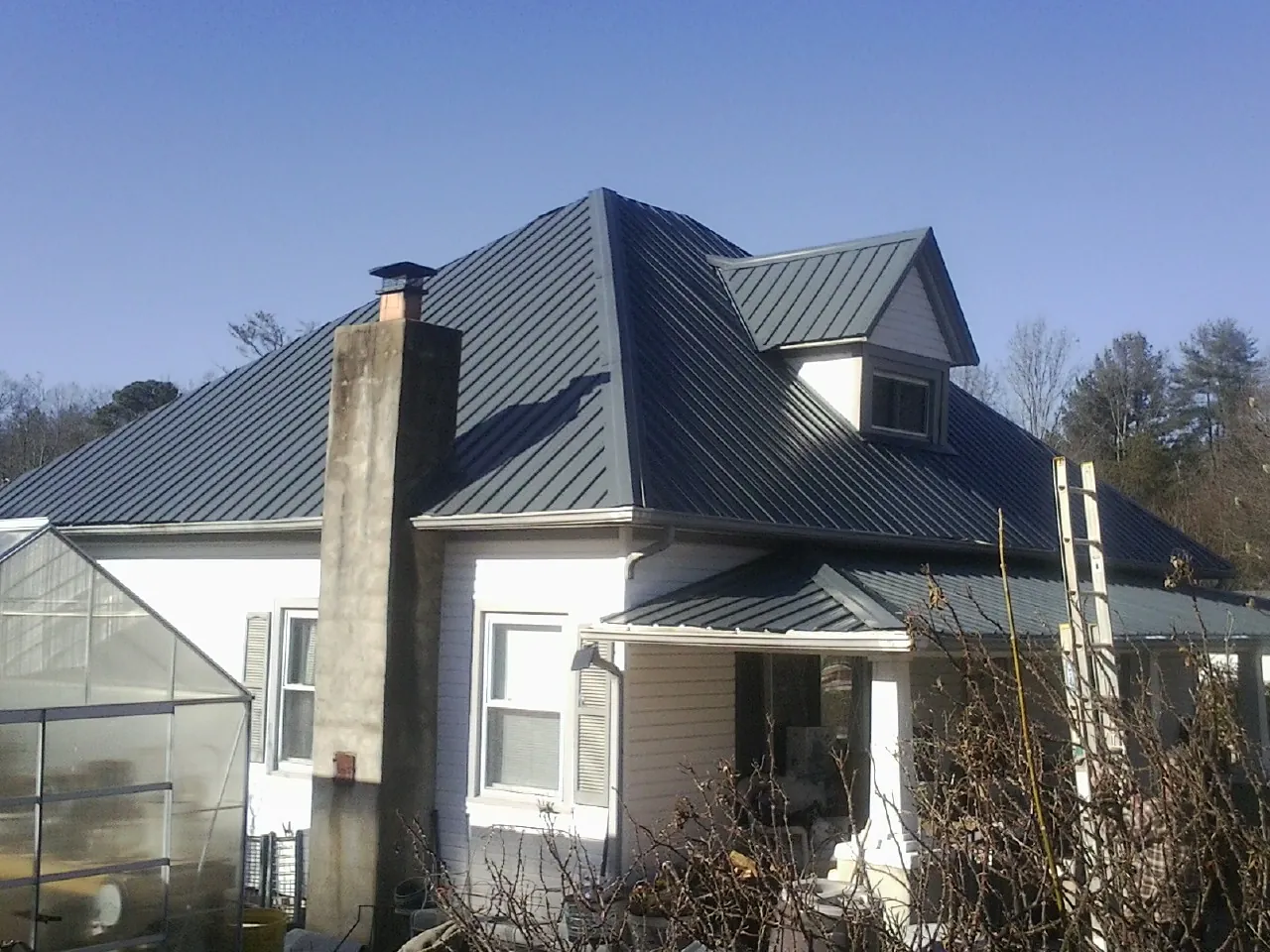 Dark blue standing seam metal roof on a white farmhouse with dormer — Slate & Tile Roof Repair by Roofing Brothers in University