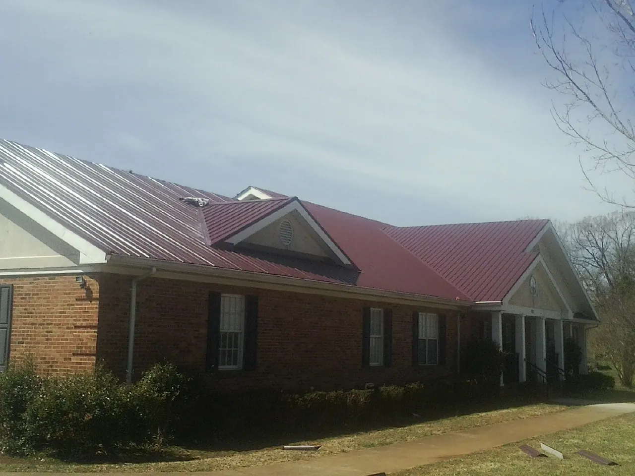 Red metal roof with gabled entries on a long brick building, from a Hail Damage Roof Repair job in University