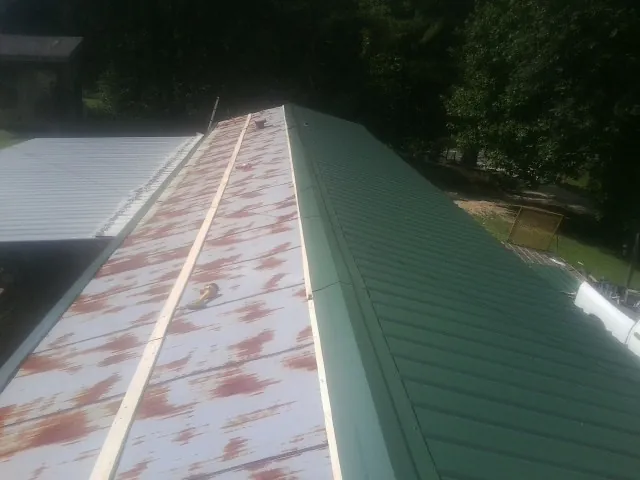 Old rusted panels beside newly installed green metal roofing — Wind Damage Roof Repair by Roofing Brothers in University