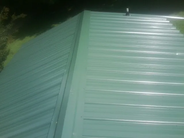 New green metal panels meeting at the ridge of a roof — Flat Roof Repair work by our crew in University