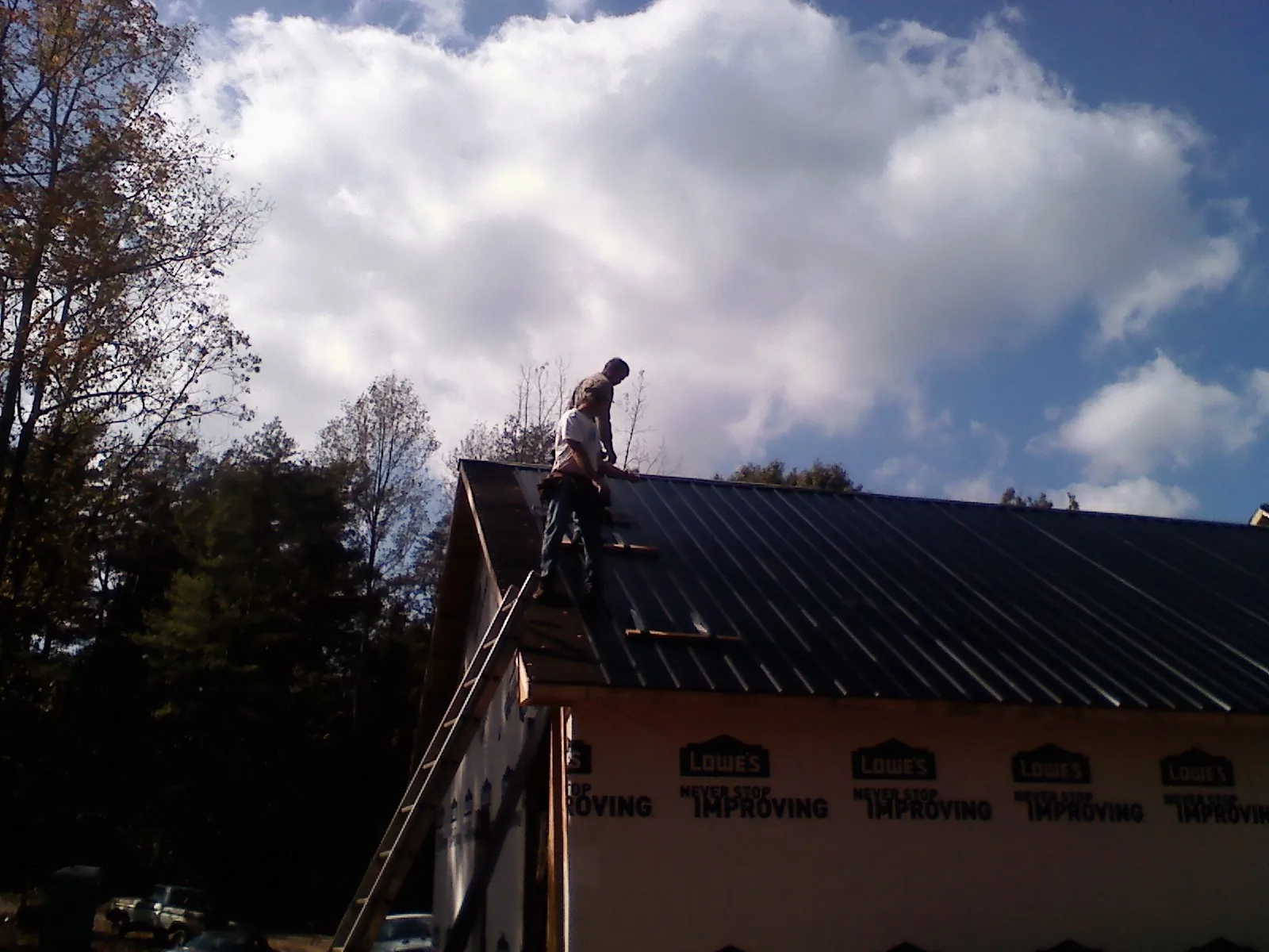Roofer fastening dark metal panels high against a cloudy sky, from a Roof Inspection job in University