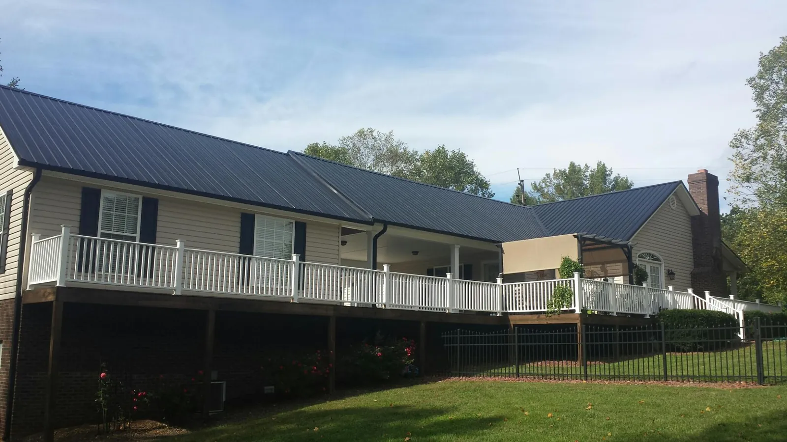 Black metal roof above a long white railed deck on a hillside home in University